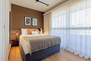 A modern hotel room with a large bed, a bedside table with a lamp, and a view of the city through sheer curtains. - Charlie Murat Vila Madalena (São Paulo)