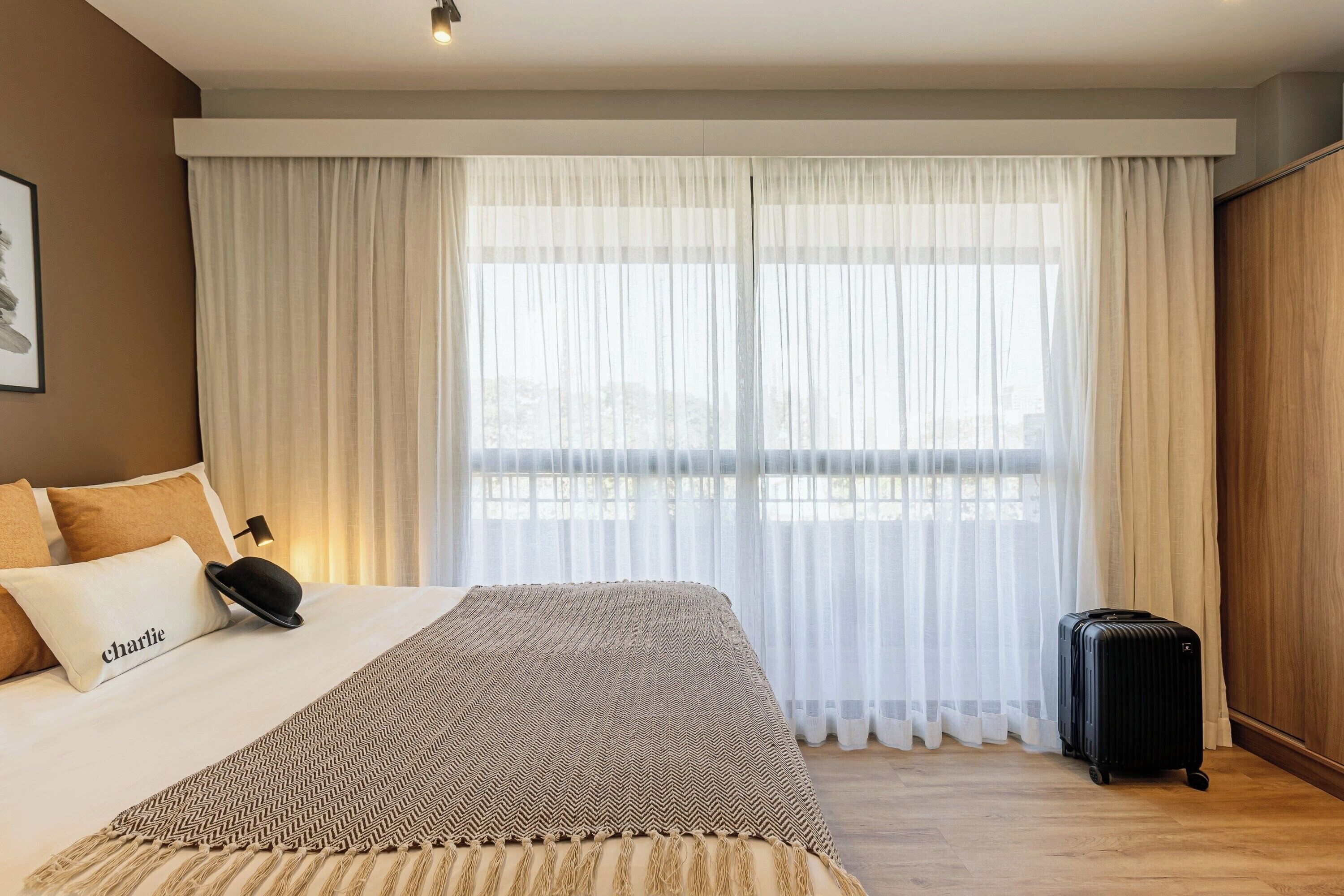 A hotel room with a bed, a suitcase, and a window with sheer curtains.