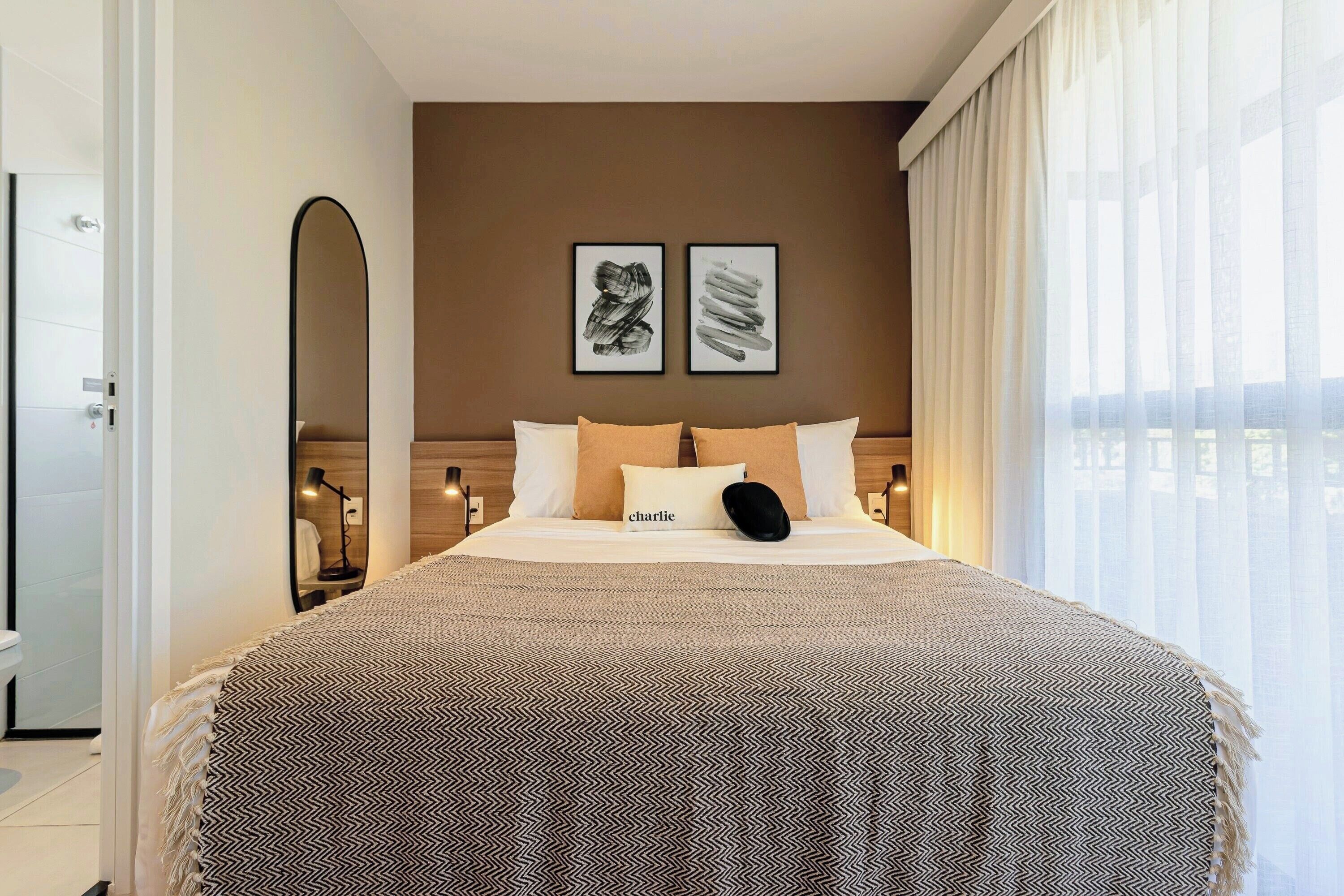 Habitación de hotel con cama, un espejo grande, dos cuadros enmarcados en la pared y vistas por la ventana.