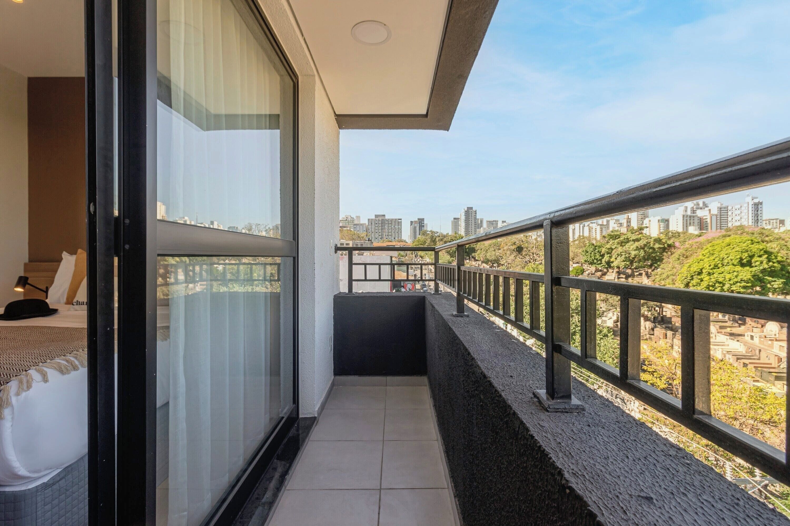 A balcony with a city view, a bed, and a window with curtains.