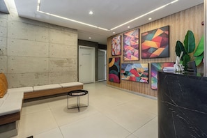 Un vestíbulo moderno con mostrador de recepción, zona de estar y arte abstracto en la pared.