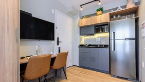 A compact kitchen with a built-in microwave, a stainless steel refrigerator, and a dining area with two chairs. - Charlie Murat Vila Madalena (São Paulo)