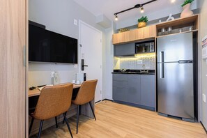 A compact kitchen with a built-in microwave, a stainless steel refrigerator, and a dining area with two chairs. - Charlie Murat Vila Madalena (São Paulo)