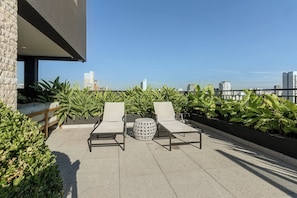 Una terraza en la azotea con dos sillones de descanso, una mesa redonda y plantas en macetas.