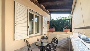 Une terrasse avec une table et des chaises, une fenêtre avec des volets et une plante en pot.