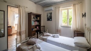 Une chambre avec deux lits, une bibliothèque, une fenêtre avec des rideaux et un appareil de climatisation.