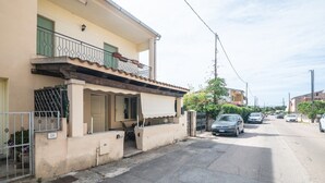 Une rue résidentielle avec une maison de couleur beige, une entrée fermée par un portail et des voitures garées.