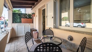 Une terrasse extérieure avec une table et des chaises, une fenêtre avec des stores et une plante en pot.