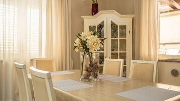 Un coin repas avec une table dressée pour quatre personnes, des chaises, un vase rempli de fleurs et un buffet aux portes vitrées.
