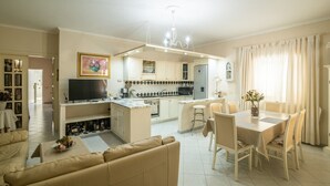 Un salon avec un canapé, un coin repas avec une table et des chaises, une cuisine équipée de placards et d’appareils électroménagers, et un téléviseur.