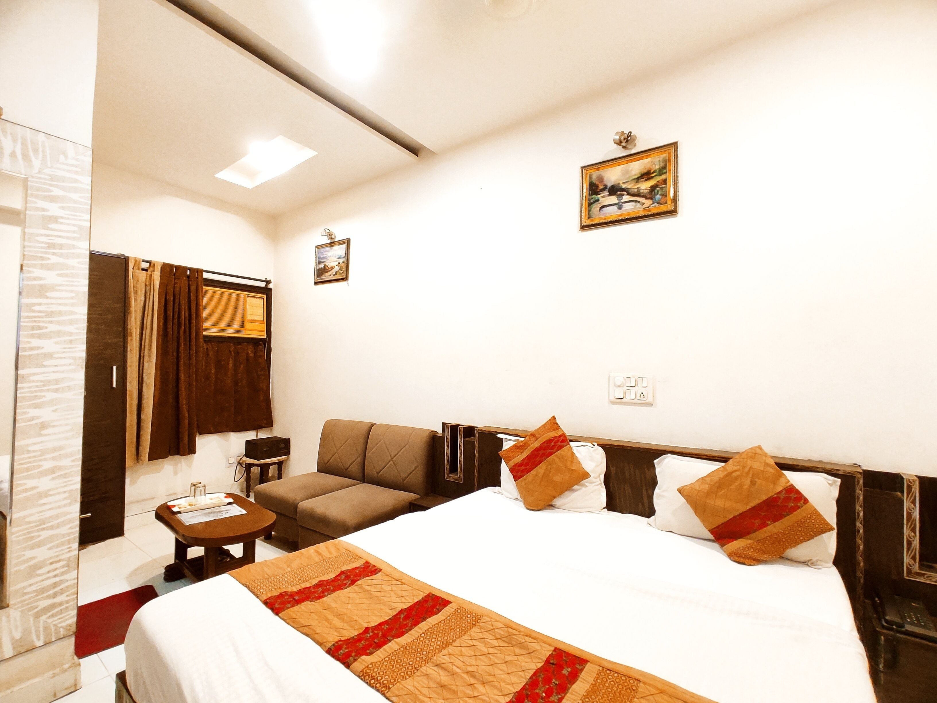 A hotel room with a bed, a sofa, a small table, and a mirror.