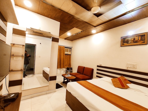 A hotel room with a bed, a small table, a chair, a mirror, and a painting on the wall.