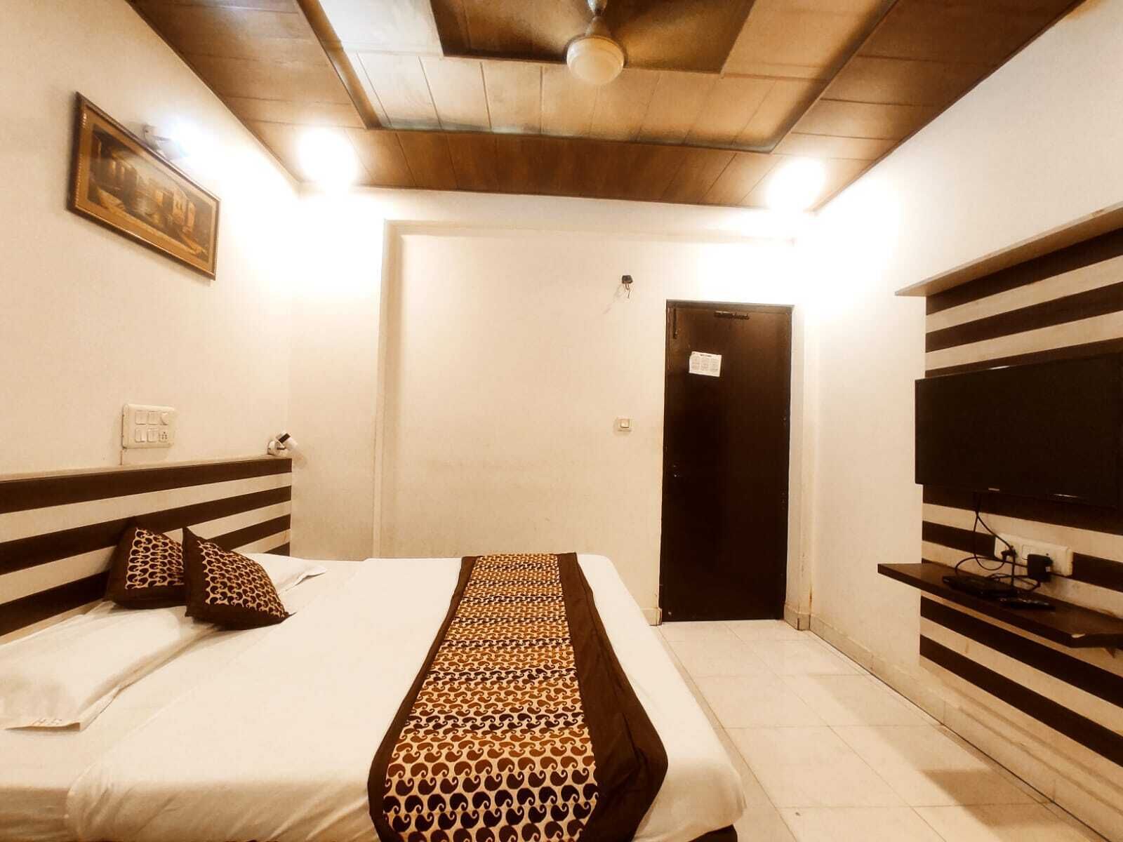 A hotel room with a bed, a television, a door, and a ceiling fan.