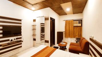 Habitación de hotel con cama, televisión montada en la pared, sofá, mesita y espejo.
