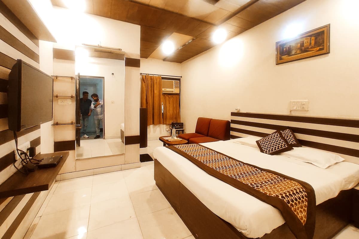 A hotel room with a bed, a sofa, a TV, a painting, and a bathroom visible through an open door.