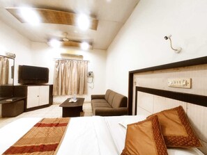 A hotel room with a bed, a sofa, a television, a desk, and a telephone.