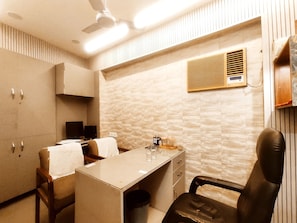 A room with a desk, chairs, a ceiling fan, a wall-mounted air conditioner, and a wardrobe.