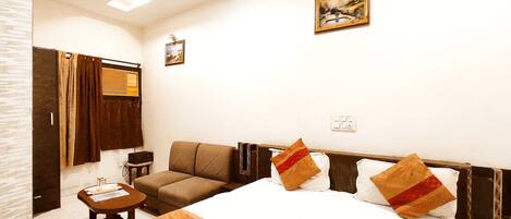 A hotel room with a bed, a sofa, a small table, a mirror, and a picture on the wall.