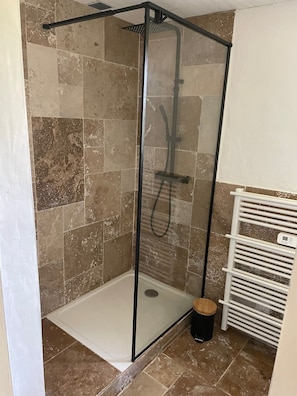 Een douche met glazen wanden, een witte betegelde vloer en een witte handdoekhouder.