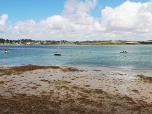 A coastal scene with boats on calm waters, a sandy beach, and a distant shoreline with houses. - Stowaway Cottage (Padstow)