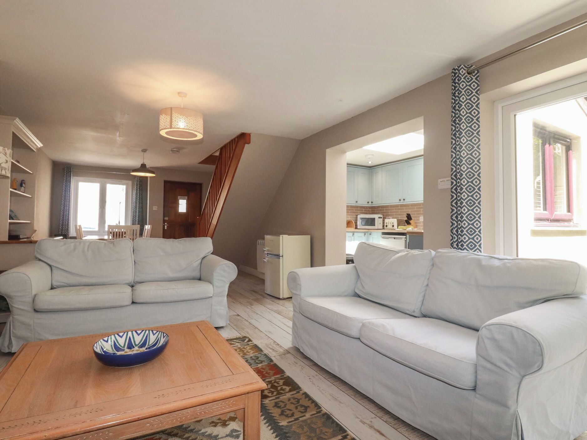 A living room with a sofa, a coffee table, and a kitchen area visible through an open door.