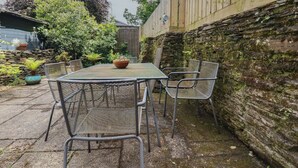 A patio with a table and chairs, surrounded by stone walls and greenery. - Stowaway Cottage (Padstow)