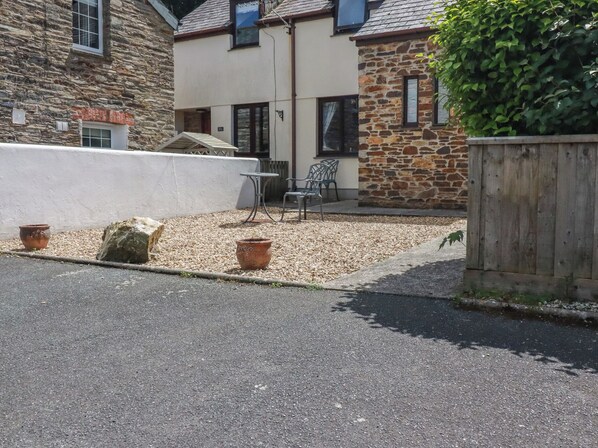 A stone building with a patio area, outdoor seating, and a wooden fence. - Stowaway Cottage (Padstow)