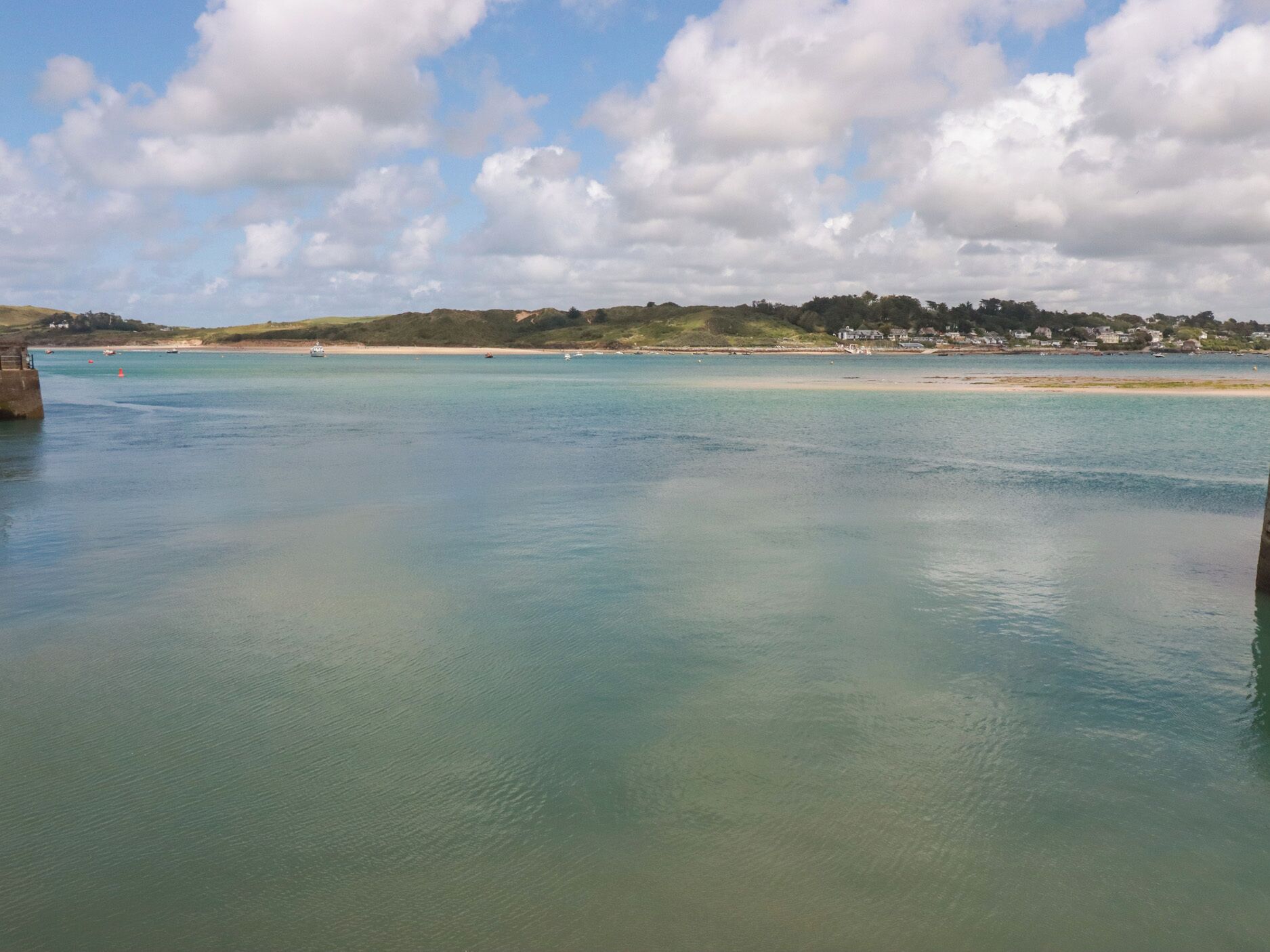 Vista costera con aguas tranquilas, una playa arenosa y una colina distante con edificios.