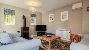 A living room with a sofa, a television, a fireplace, a table, and a patterned rug. - Stowaway Cottage (Padstow)