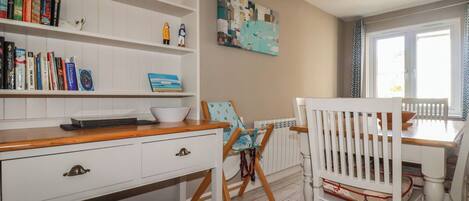 A room with a white bookshelf, a dining table with chairs, a radiator, and a window.