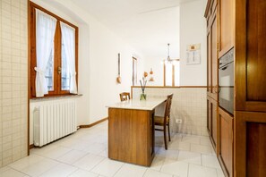 A kitchen with a wooden island, white tiled walls, a window with curtains, and a hanging light fixture.