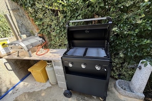 A portable gas grill with a black finish, a yellow container, and a stone structure in the background.