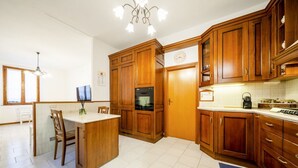 A kitchen with wooden cabinets, a central island, a clock, and a coffee maker. - A few minutes from Lake Como (Sun Tower) (Calolziocorte)
