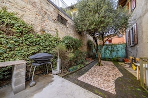 Un muro de piedra, un árbol, una parrilla y un sendero en un patio.