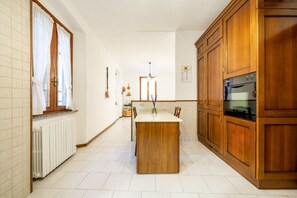 Una cucina con mobili in legno, un'isola centrale, un piano di lavoro bianco e una finestra con tende.