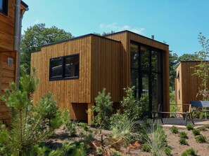 Eine moderne Holzblockhütte mit einem großen Fenster, umgeben von viel Grün.