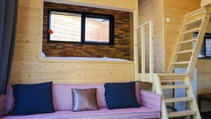 A wooden cabin interior with a pink sofa, a window with blinds, and a wooden ladder. - Holiday Home in Arnhem With Terrace (Arnhem)