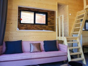 Ein Holzblockhaus-Interieur mit einem rosa Sofa, einem Fenster mit Jalousien und einer Holzleiter.