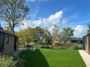 Ein gepflegter Rasen mit einer Terrassenfläche, umgeben von Bäumen und Gebäuden.