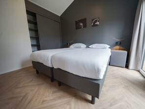 Ein modernes Schlafzimmer mit Bett, Nachttisch, Lampe und einem Fenster mit Vorhängen.