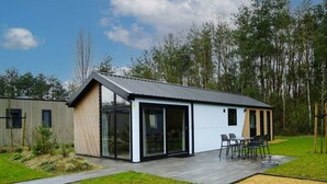A modern house with a large glass door, a patio with outdoor furniture, and a surrounding garden. - Holiday Home in Belfeld With Terrace (Belfeld)