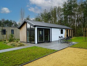 Ein modernes Haus mit einer großen Glasdoor, einer Terrasse mit Gartenmöbeln und einem umlaufenden Garten.