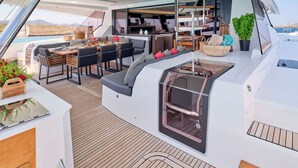Das Deck einer Yacht mit Essbereich, Grill und Sitzgelegenheit mit Kissen.