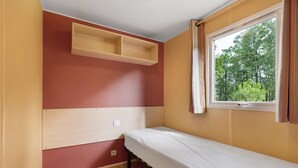 Una habitación pequeña con una cama individual, una ventana con cortinas y una repisa sobre la cama.