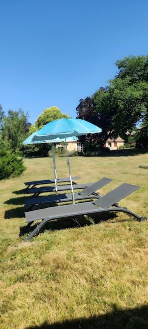 A grassy outdoor area with a blue umbrella and metal chairs. - Bungalow "À l'Orée des Bois" with Shared Pool, Wi-Fi, and Air Conditioning (Monfaucon)
