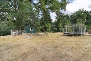 A small green building with a window, surrounded by trees and a grassy area.