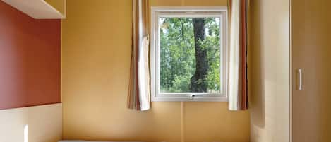 Ein Zimmer mit einem Bett, einem fensterbelaubten Fenster und Blick auf Bäume.