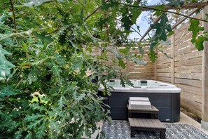 A hot tub with a wooden deck and a pergola with oak leaves.