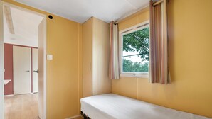 Una habitación con cama, ventana con cortinas, una puerta y vista a árboles desde afuera.