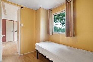 A room with a bed, a window with curtains, a door, and a view of trees outside.